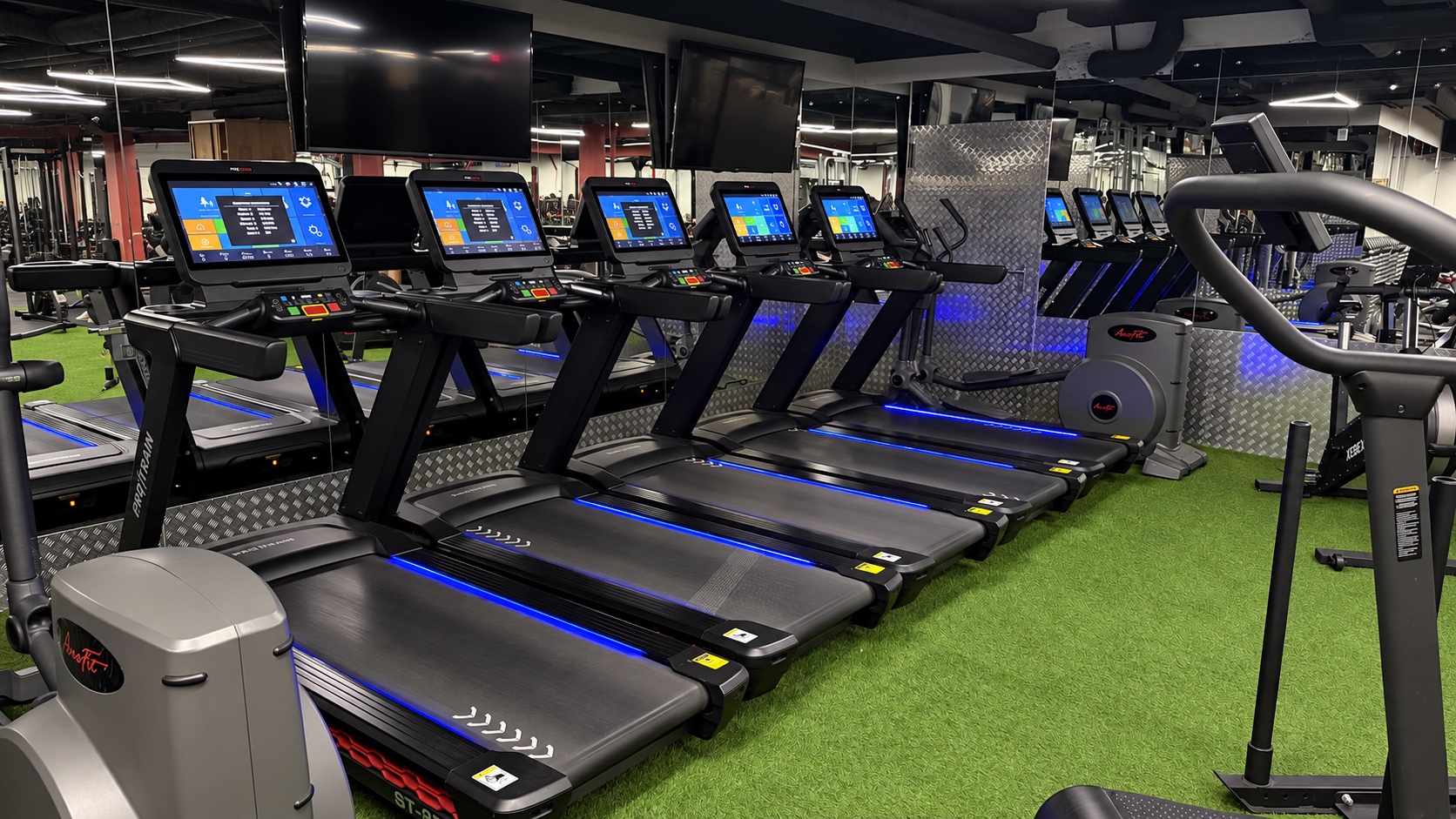 Ряд беговых дорожек с экранами и синей подсветкой в кардиозоне IRON FITNESS