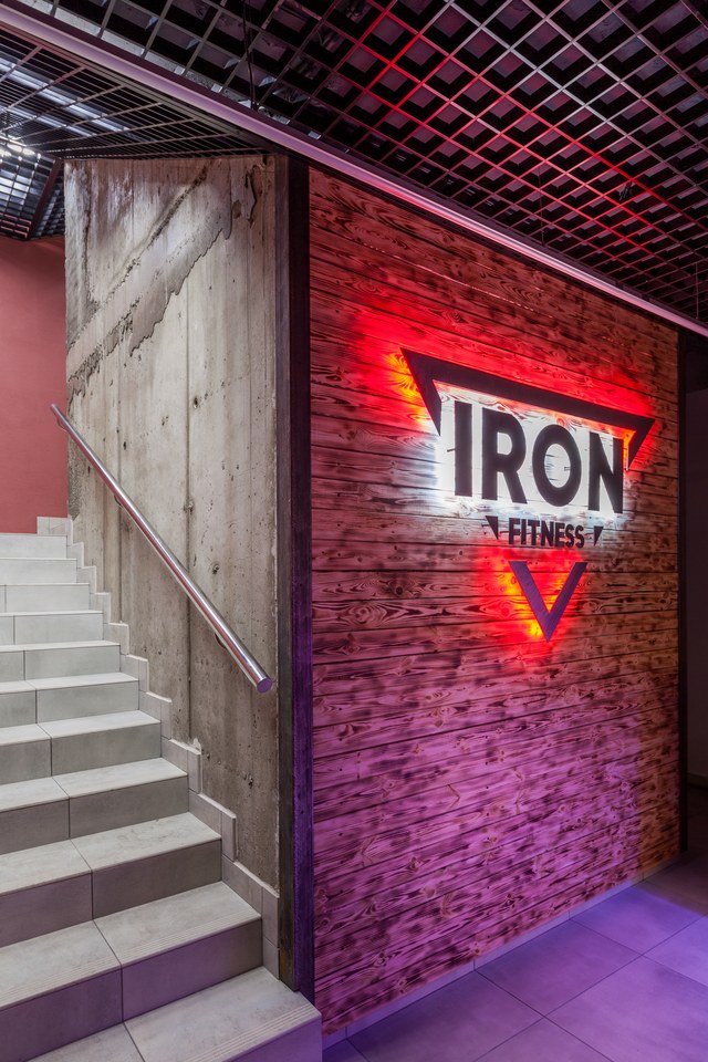 Подсвеченный логотип IRON FITNESS на деревянной стене у входа